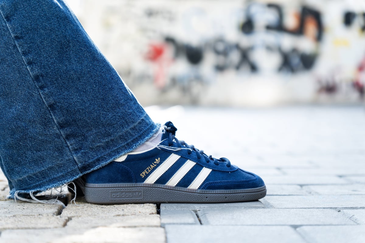 Close-up of blue sneakers and frayed denim against a graffiti wall
