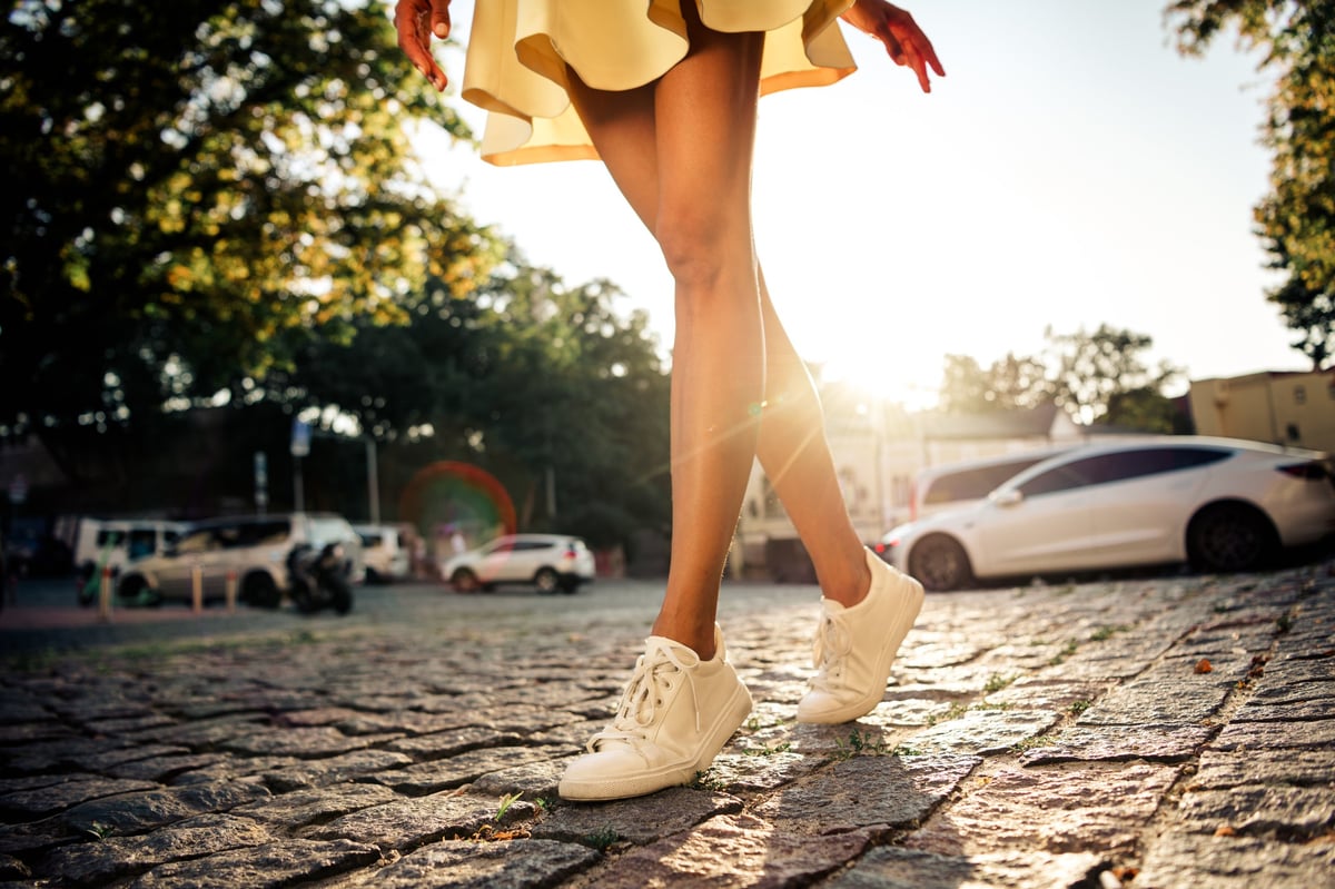Woman walking in white sneakers across sunlit cobblestones